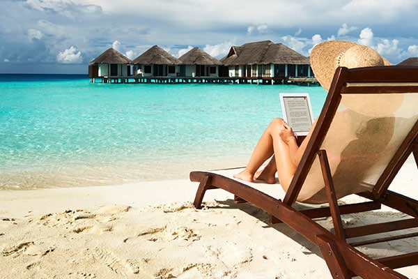 Woman on beach relaxing on chair reading e-book